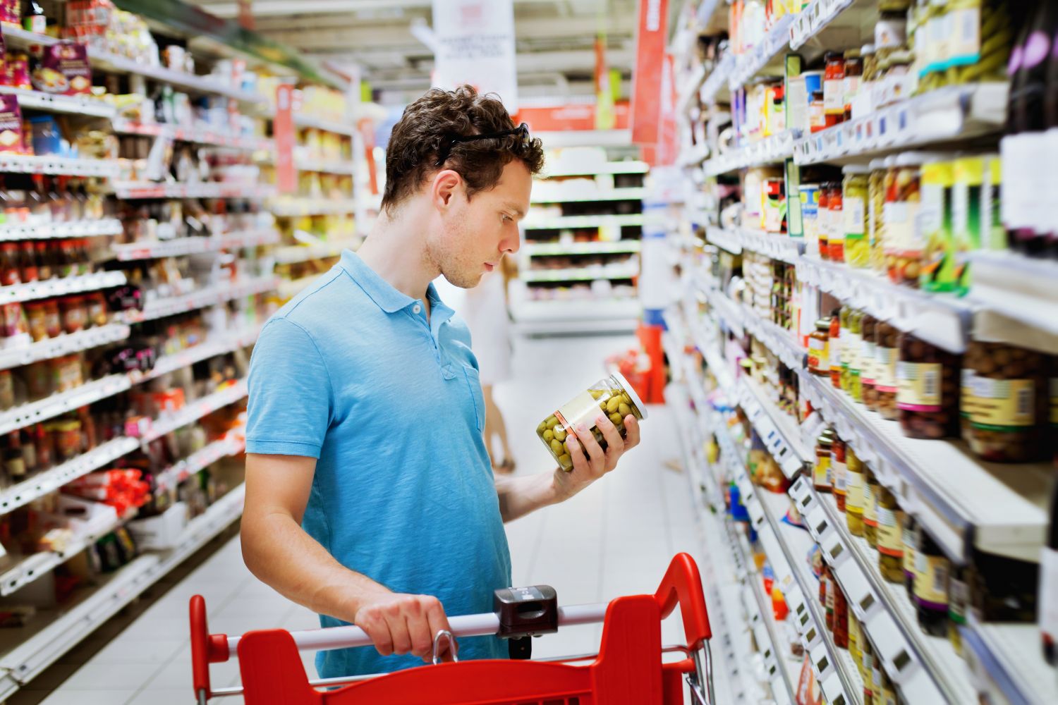 Ein Mann im Supermarkt schaut sich ein Olivenglas an. Thema: Wettbewerbsvorteile
